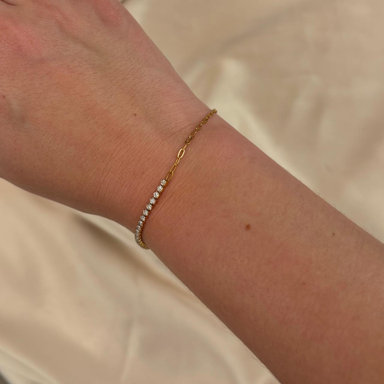 Gold bracelet with small diamonds on a wrist against a neutral background